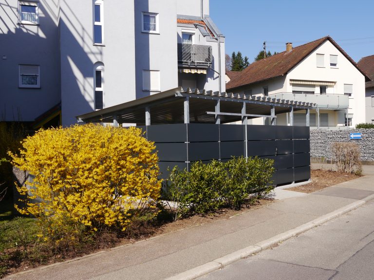 Mülleinhausung mit Schiebetür vor einer Wohnanlage